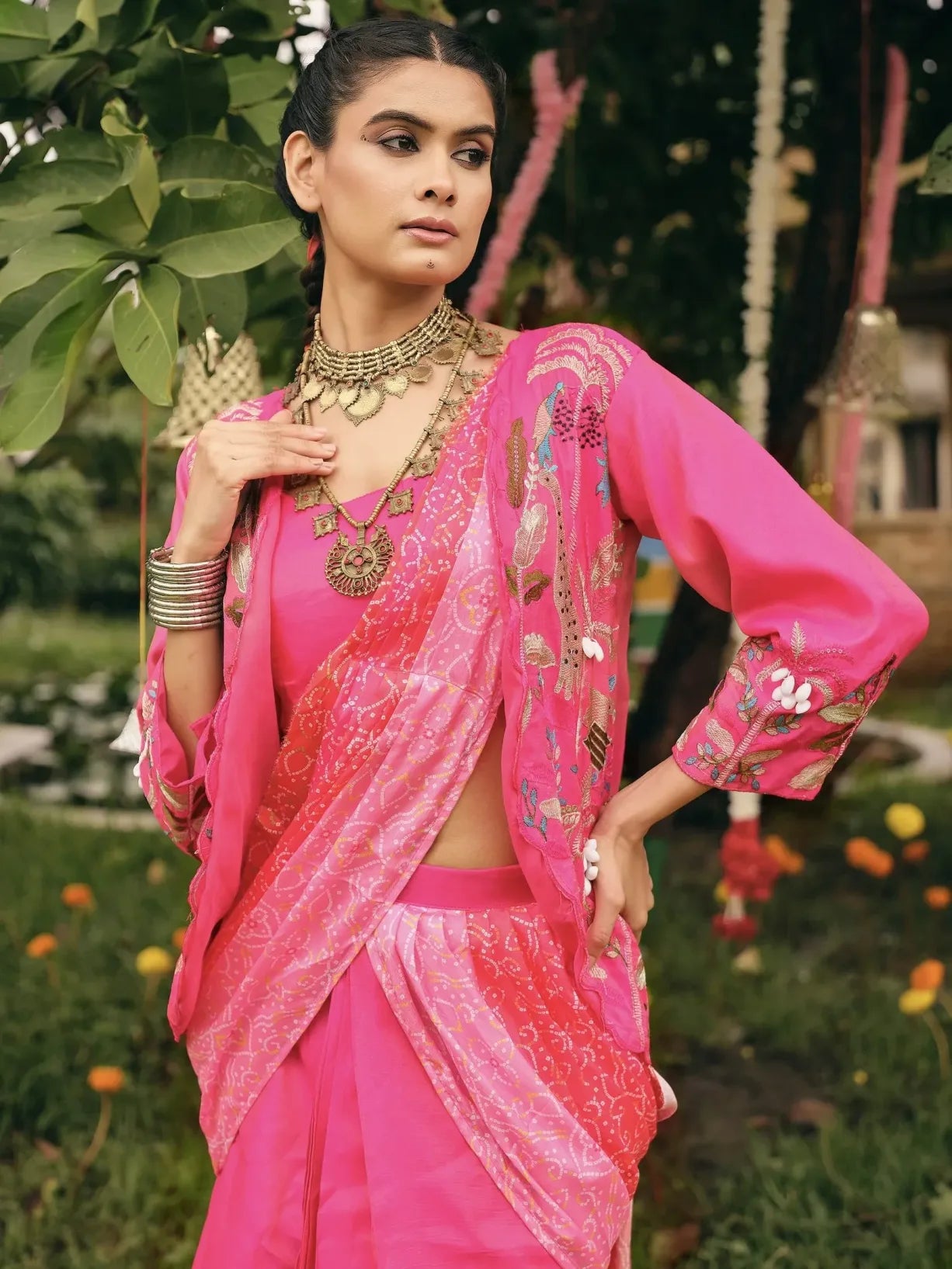 Woman in a pink saree with intricate designs standing outdoors.