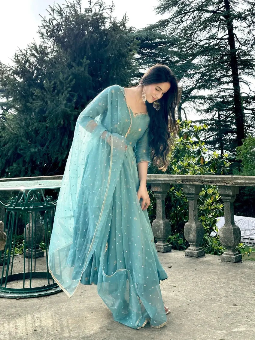 Woman in a light blue saree standing outdoors with greenery in the background