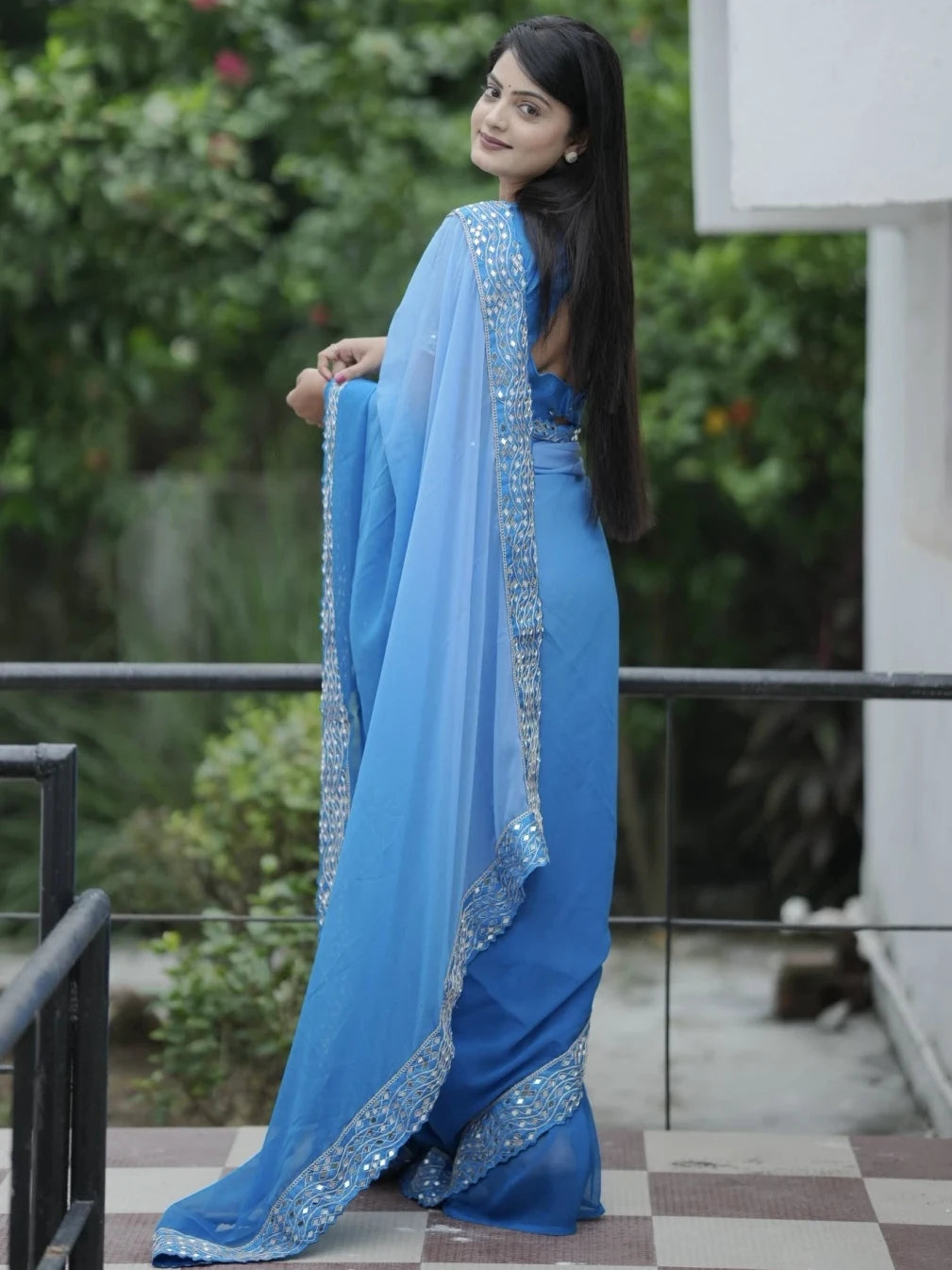 Woman wearing a blue saree with a white border outdoors.