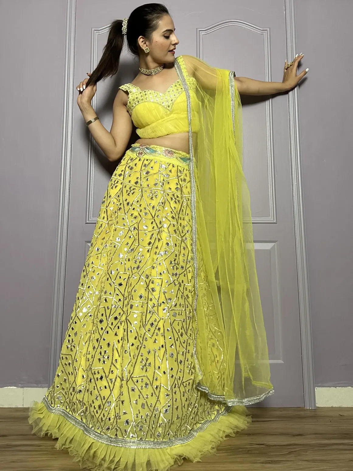 Woman in a yellow traditional outfit with a matching dupatta against a plain background