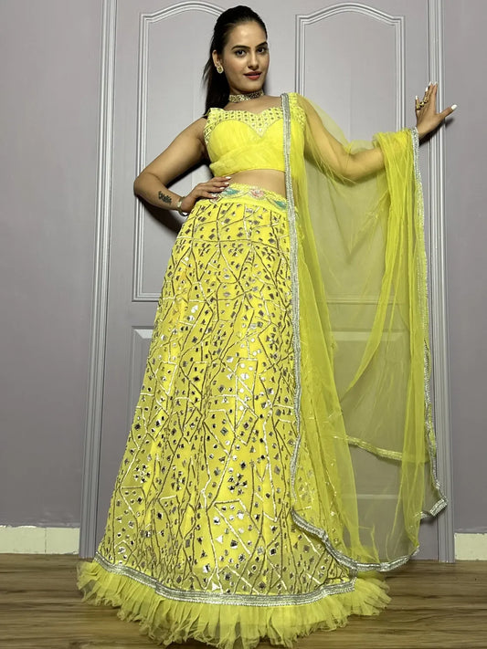 Woman in a bright yellow traditional outfit with a matching dupatta against a plain background