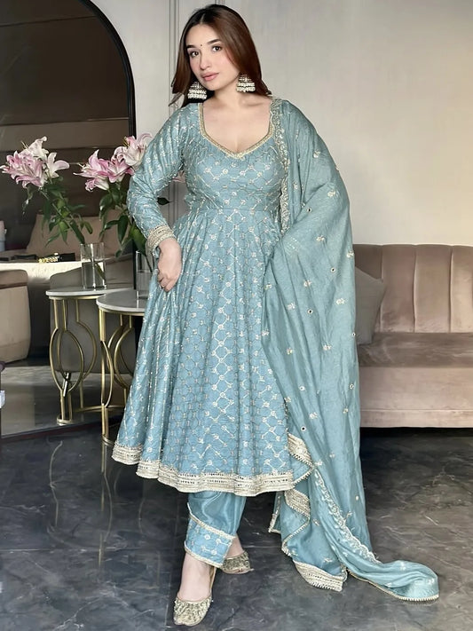 Woman in a light blue traditional outfit standing in a modern living room.