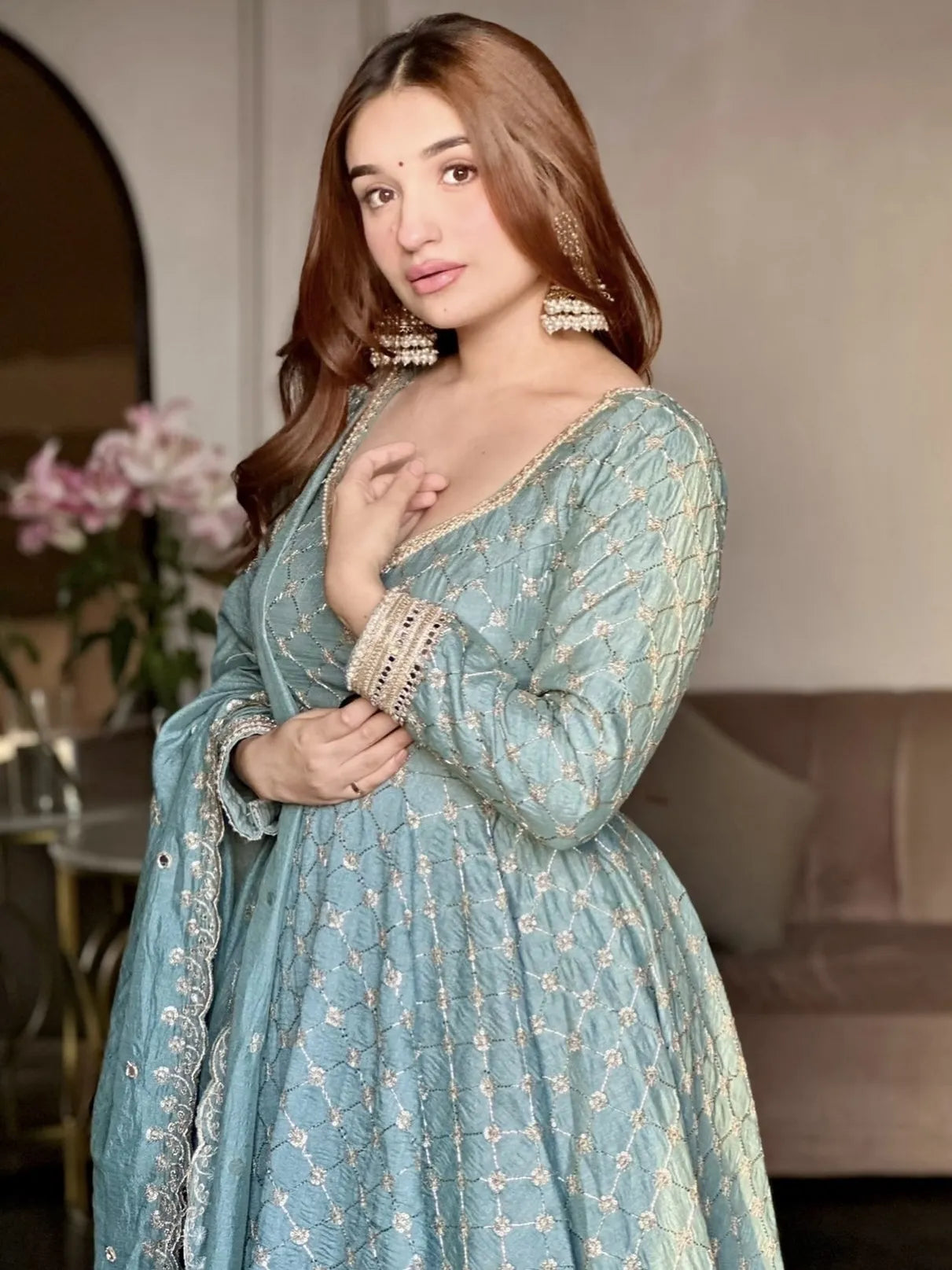 Woman in a light blue traditional outfit with floral patterns indoors.