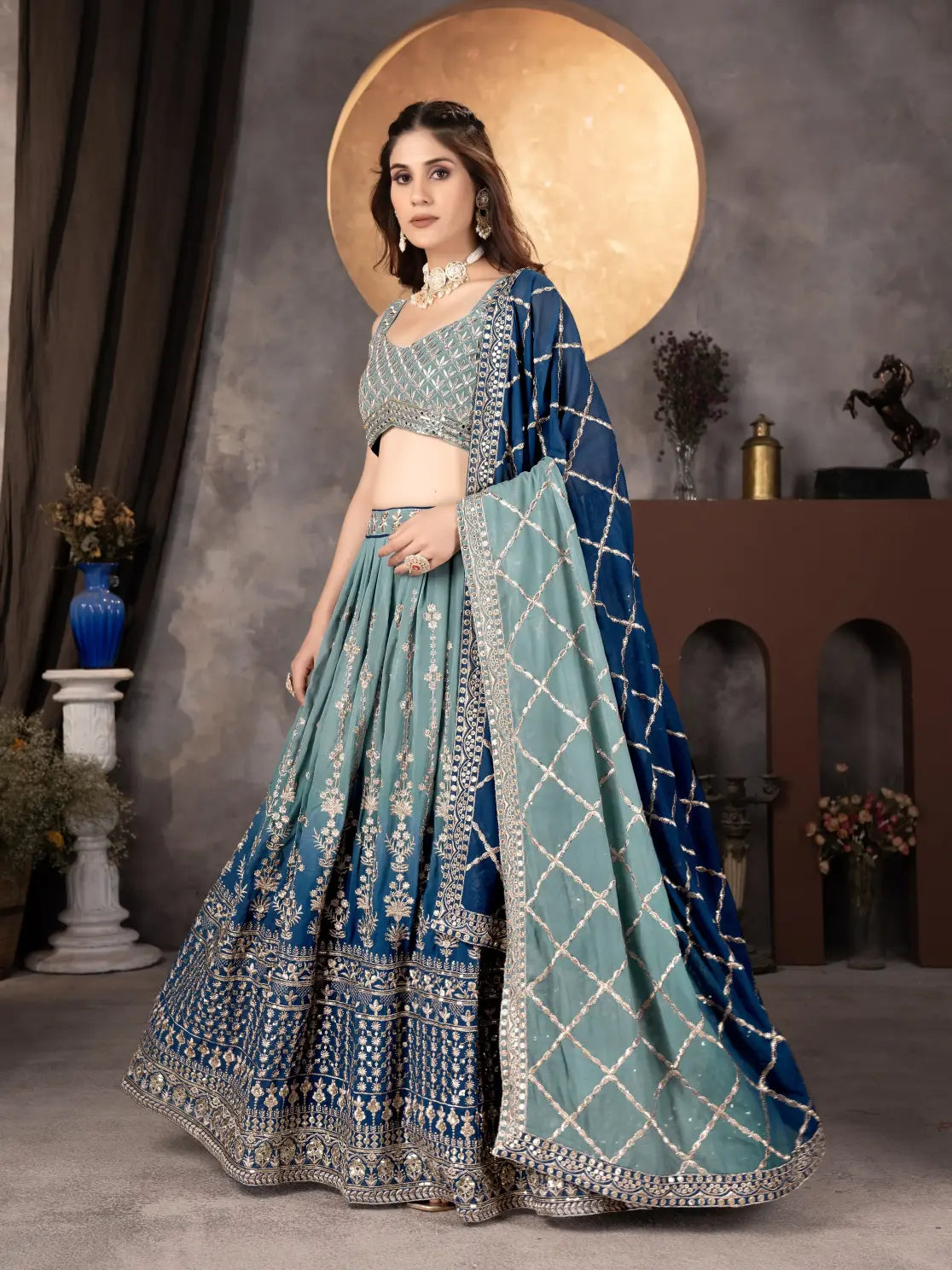 Woman in a traditional blue and green embroidered lehenga with a gold background