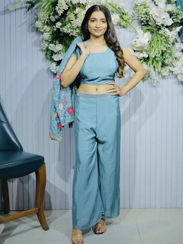Woman in a blue traditional outfit standing in front of floral decorations.