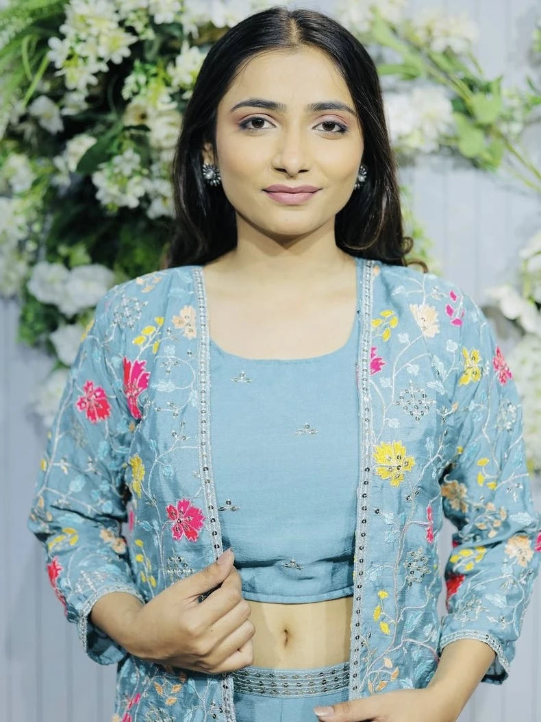 Woman wearing a light blue traditional outfit with floral embroidery against a floral background