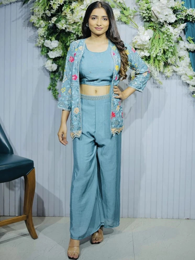 Woman in a blue outfit with floral embroidery standing in front of floral decorations.