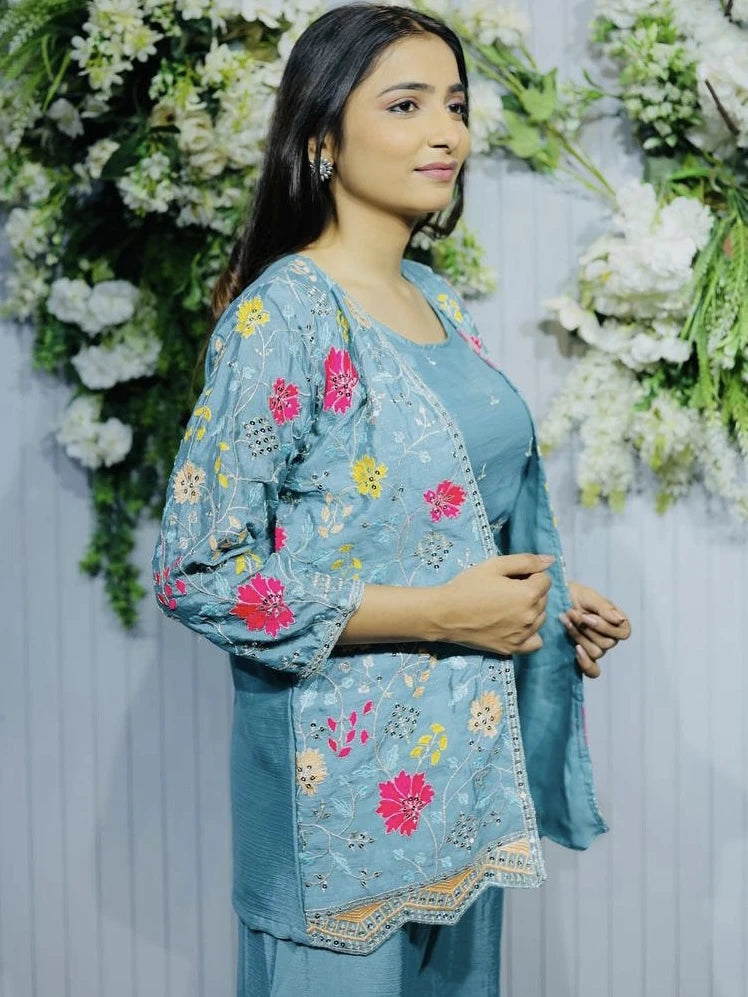 Woman wearing a blue embroidered outfit with floral patterns against a floral backdrop