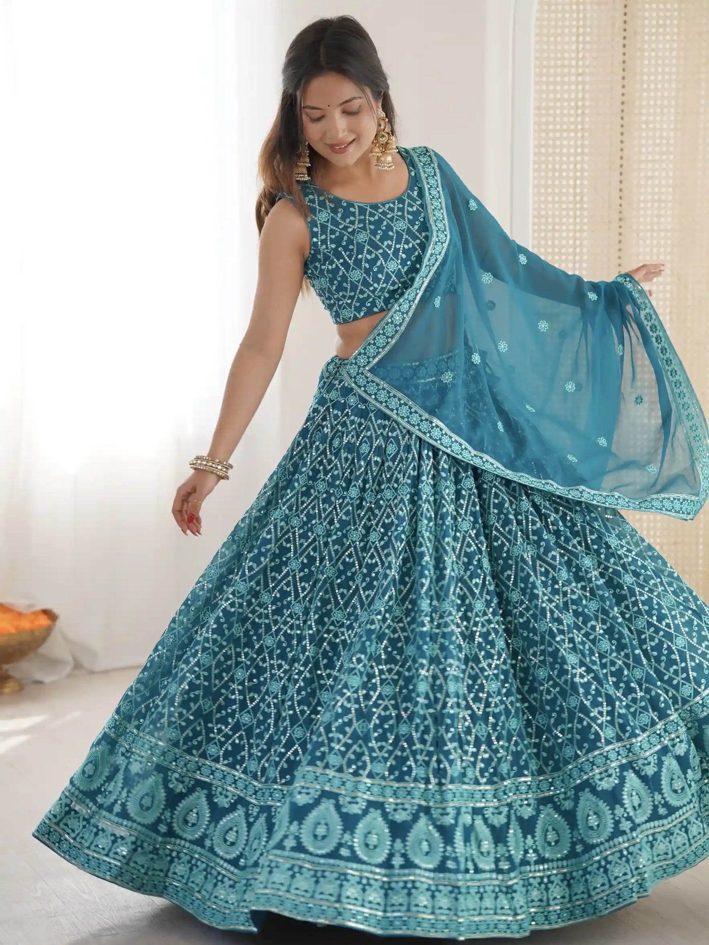 Woman wearing a teal traditional outfit with a matching dupatta in a bright room.