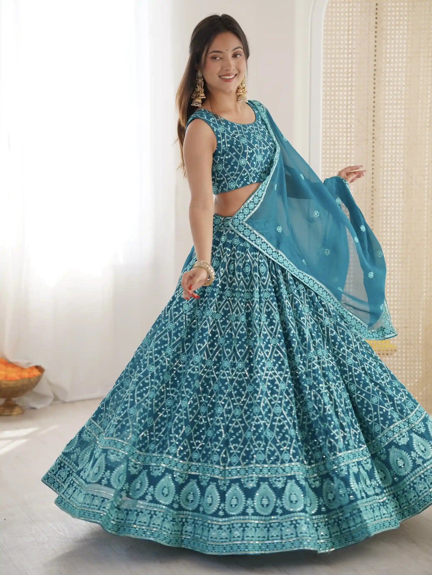 Woman wearing a teal embroidered lehenga with a matching dupatta against a neutral background