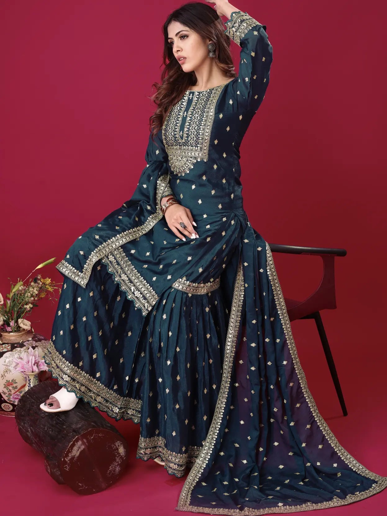 Woman in a traditional blue embroidered outfit sitting on a red background