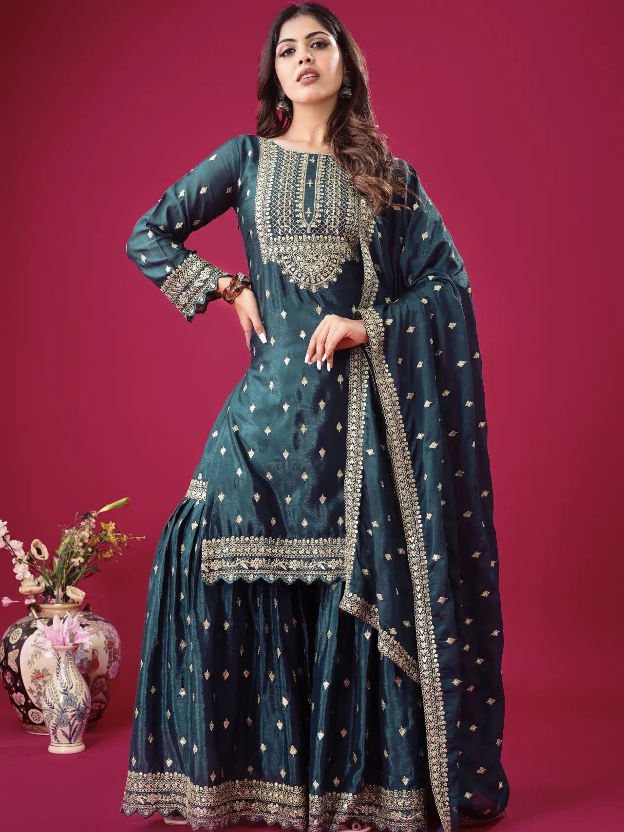 Woman wearing a traditional teal dress with intricate patterns on a pink background