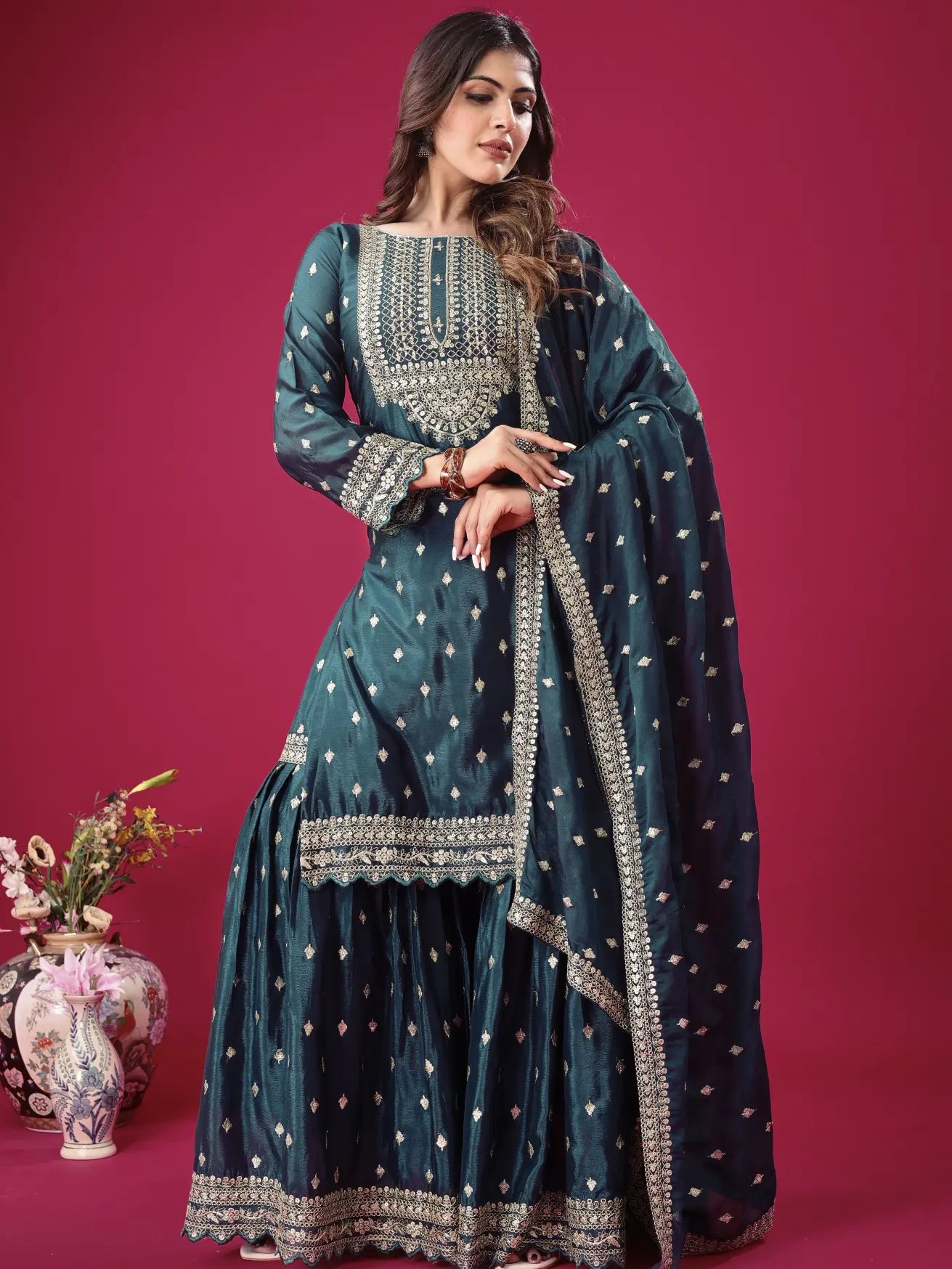 Woman wearing a teal embroidered traditional outfit on a pink background
