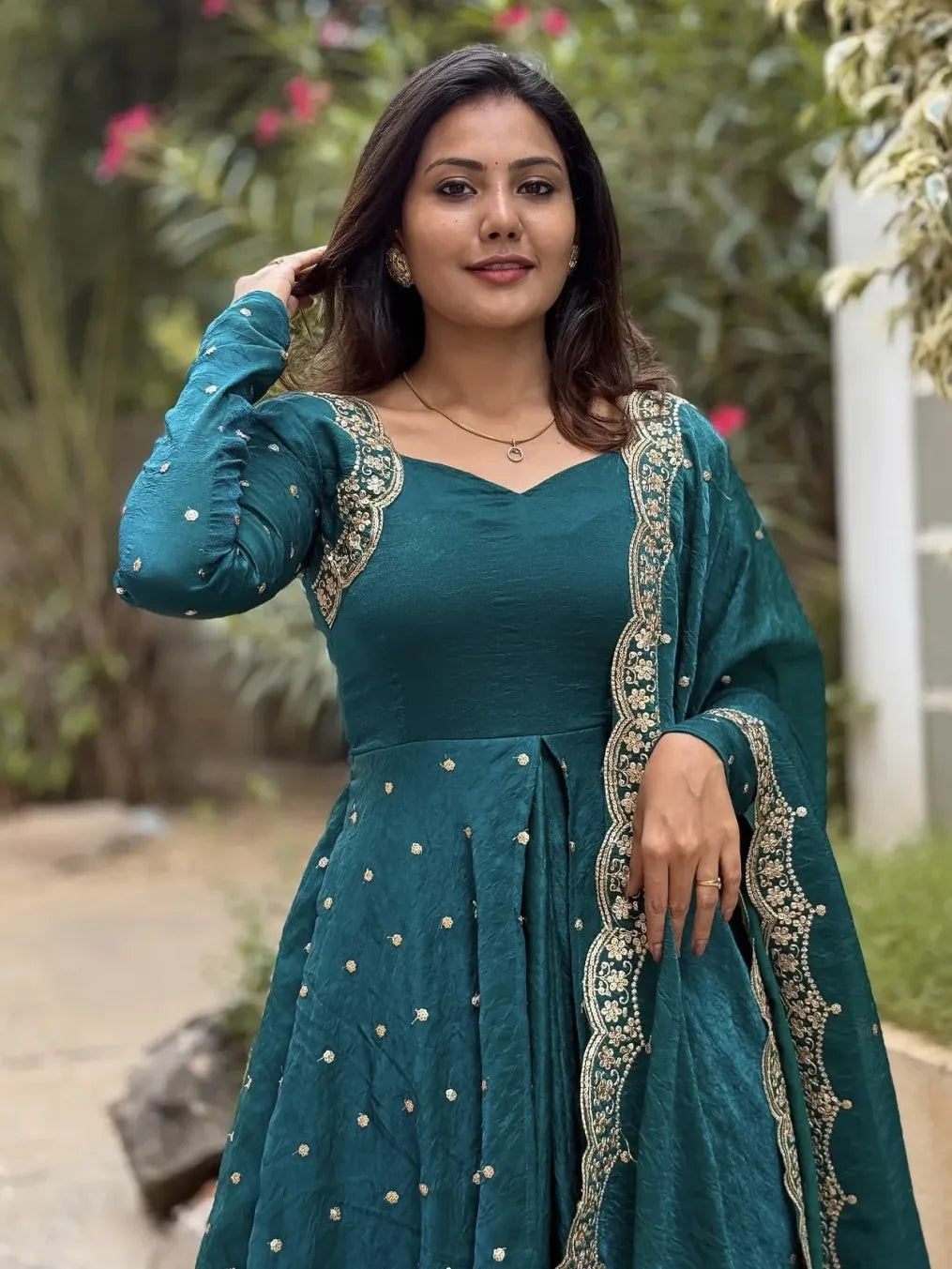 Woman wearing a teal traditional outfit with intricate designs outdoors.