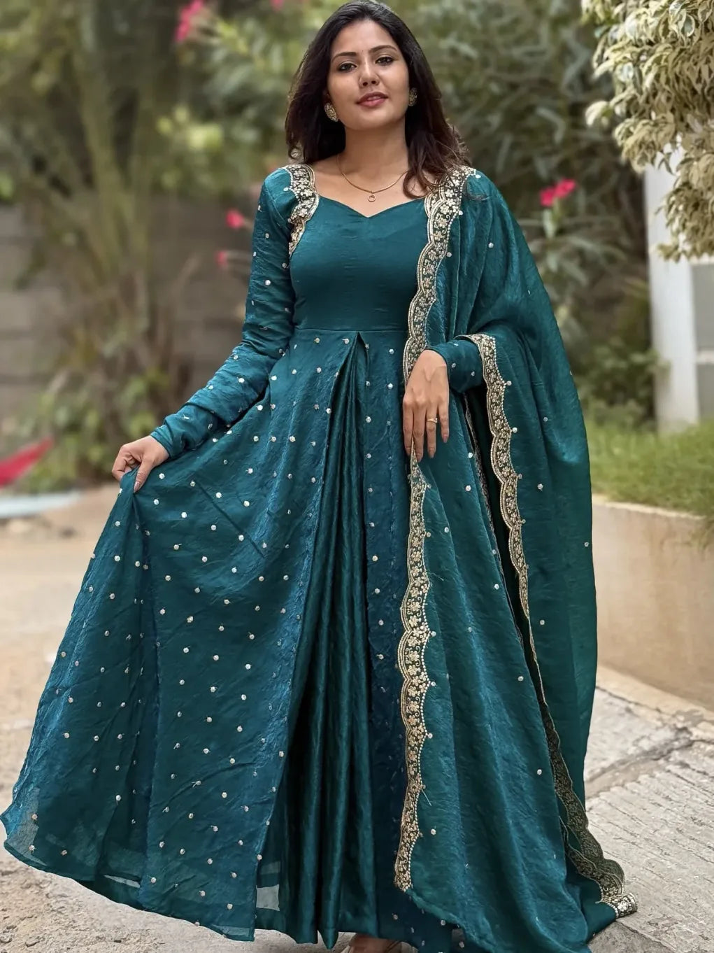 Woman wearing a teal traditional outfit with intricate designs outdoors.