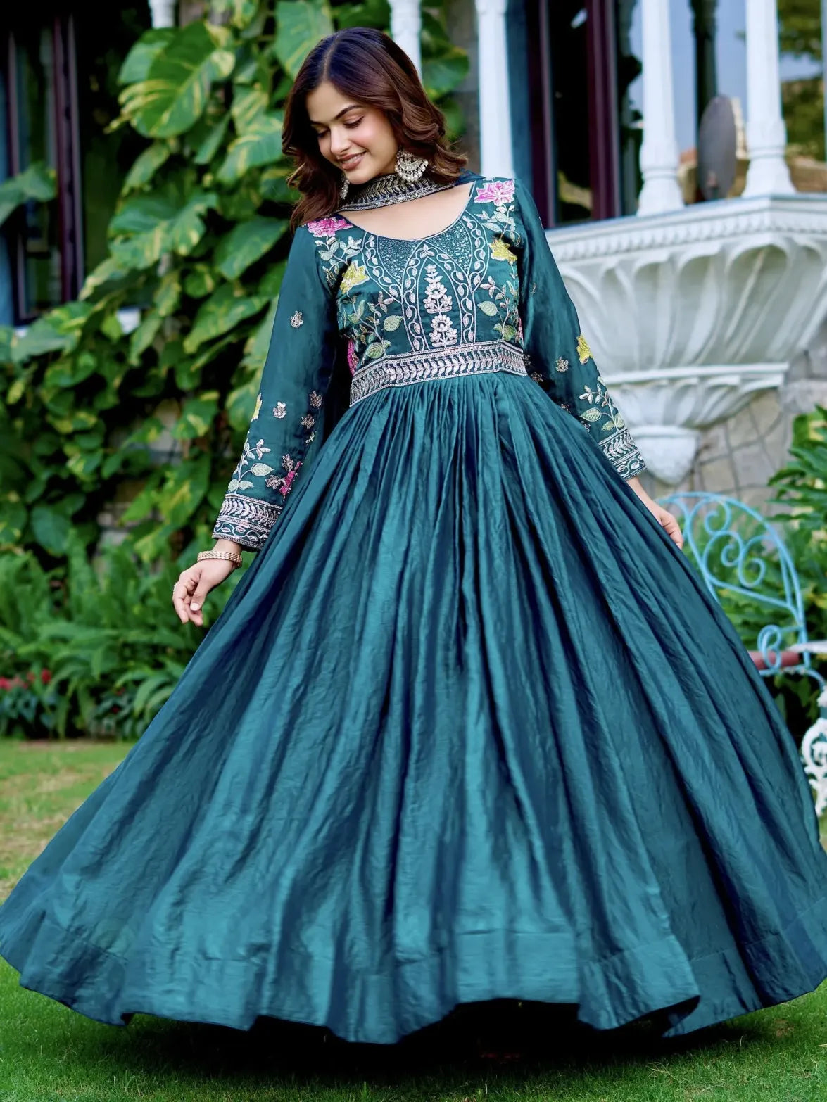 Woman wearing a teal embroidered dress outdoors with greenery in the background