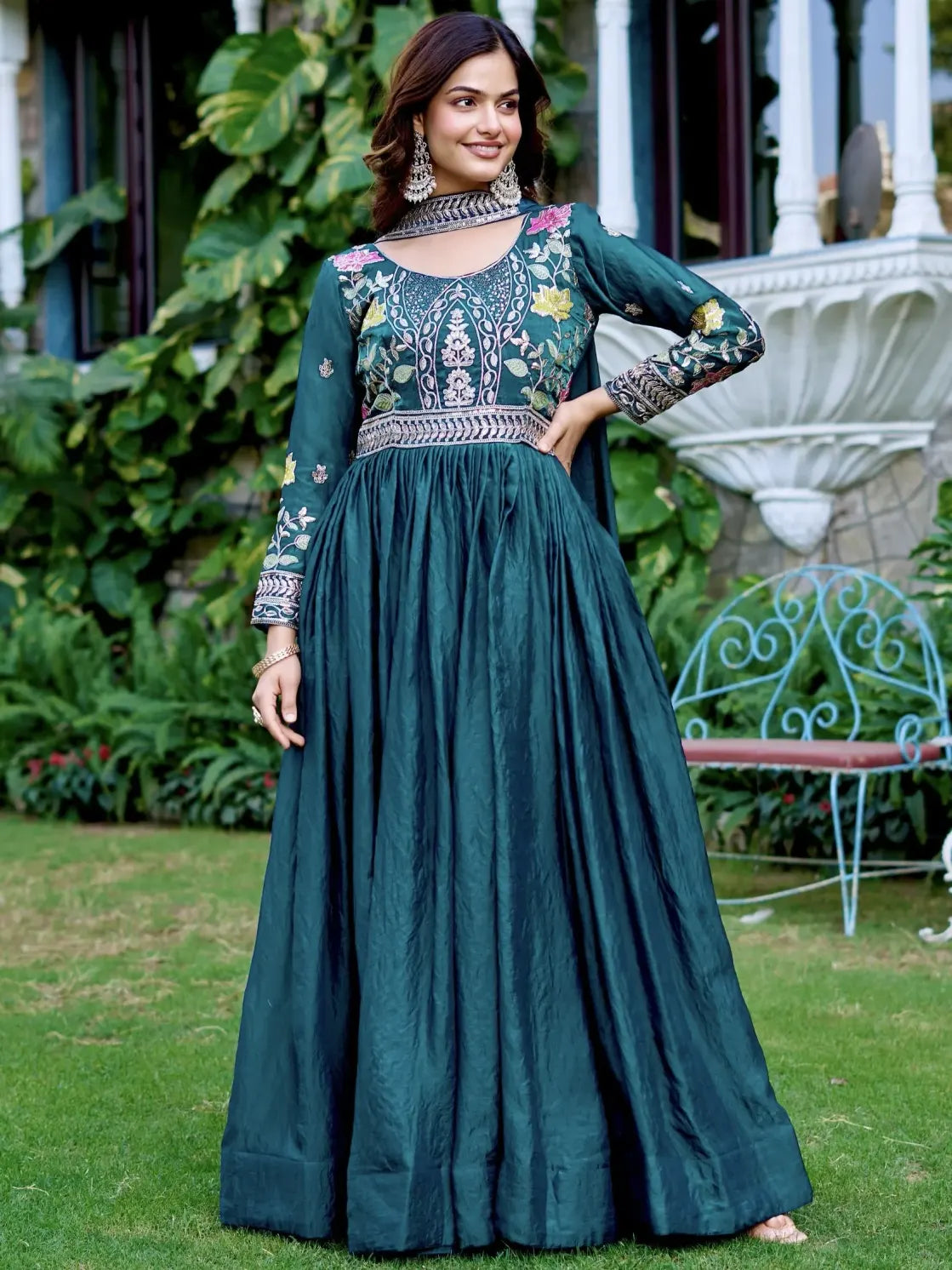 Woman wearing a teal embroidered dress standing outdoors with greenery in the background