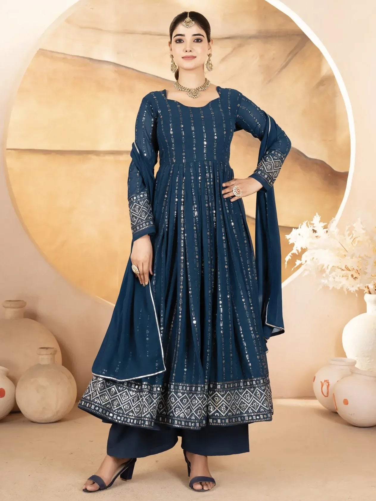 Woman wearing a blue traditional outfit with intricate patterns against a beige background