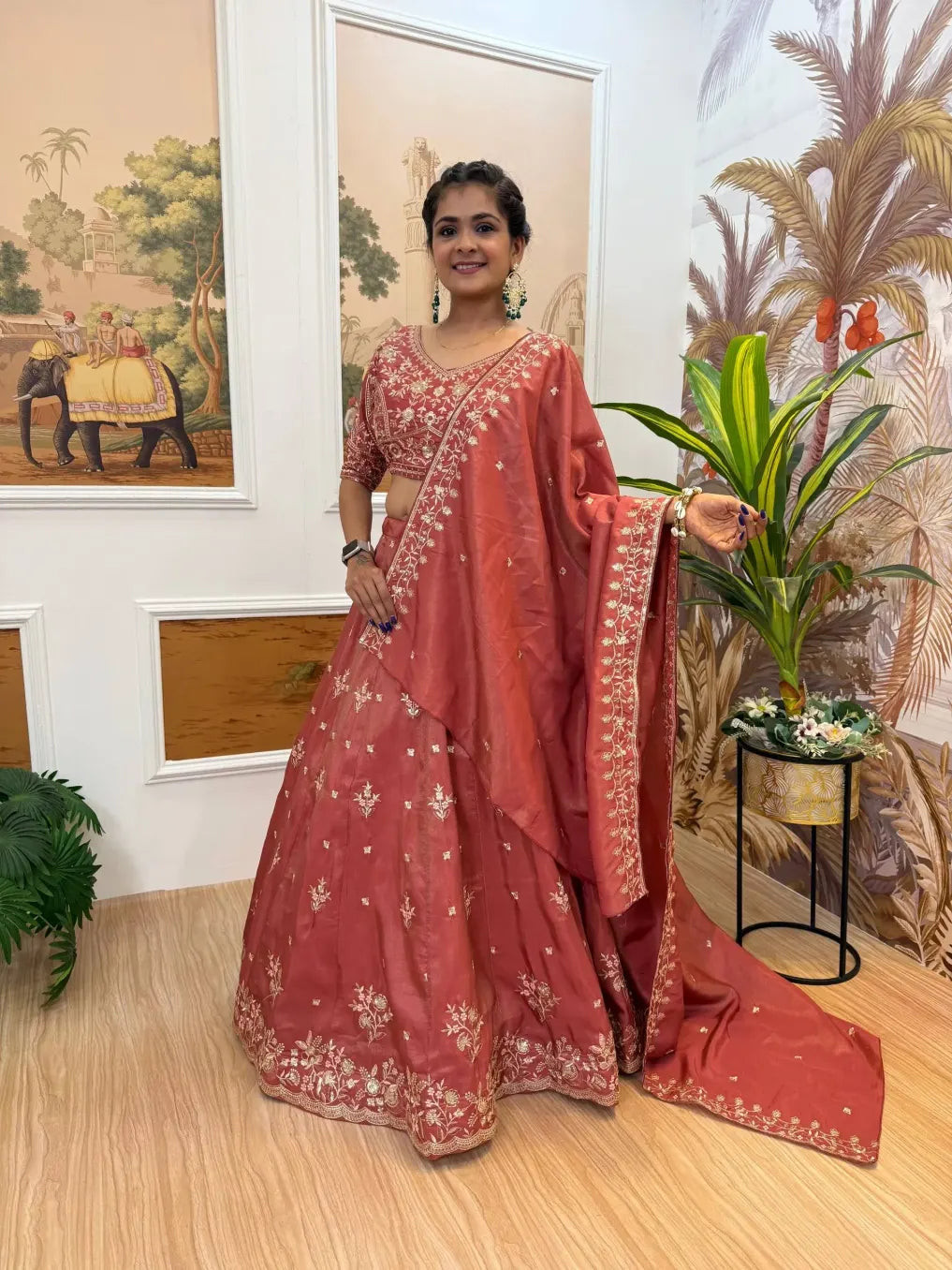 Woman in a red saree standing indoors with decorative elements in the background