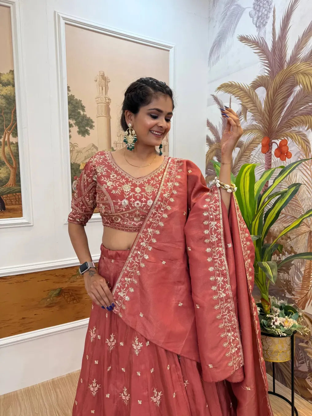 Woman in a traditional pink embroidered outfit standing indoors with decorative elements.