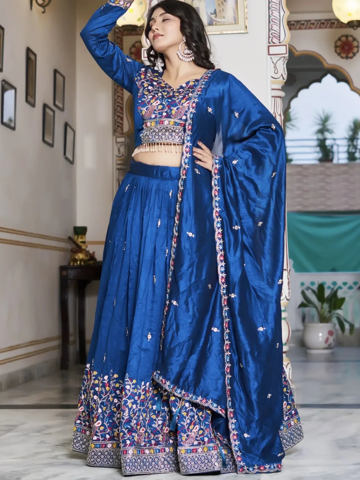 Woman wearing a traditional blue outfit with floral patterns indoors.