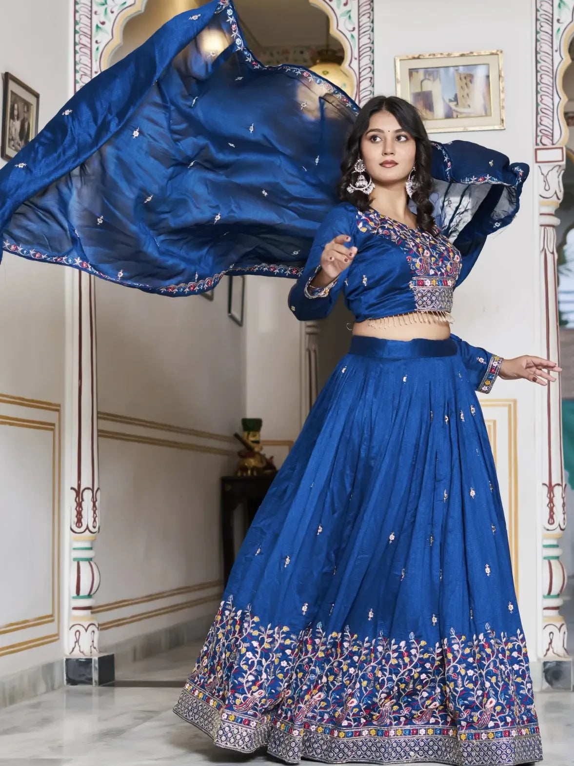 Woman in a blue traditional outfit with intricate designs in an ornate room.