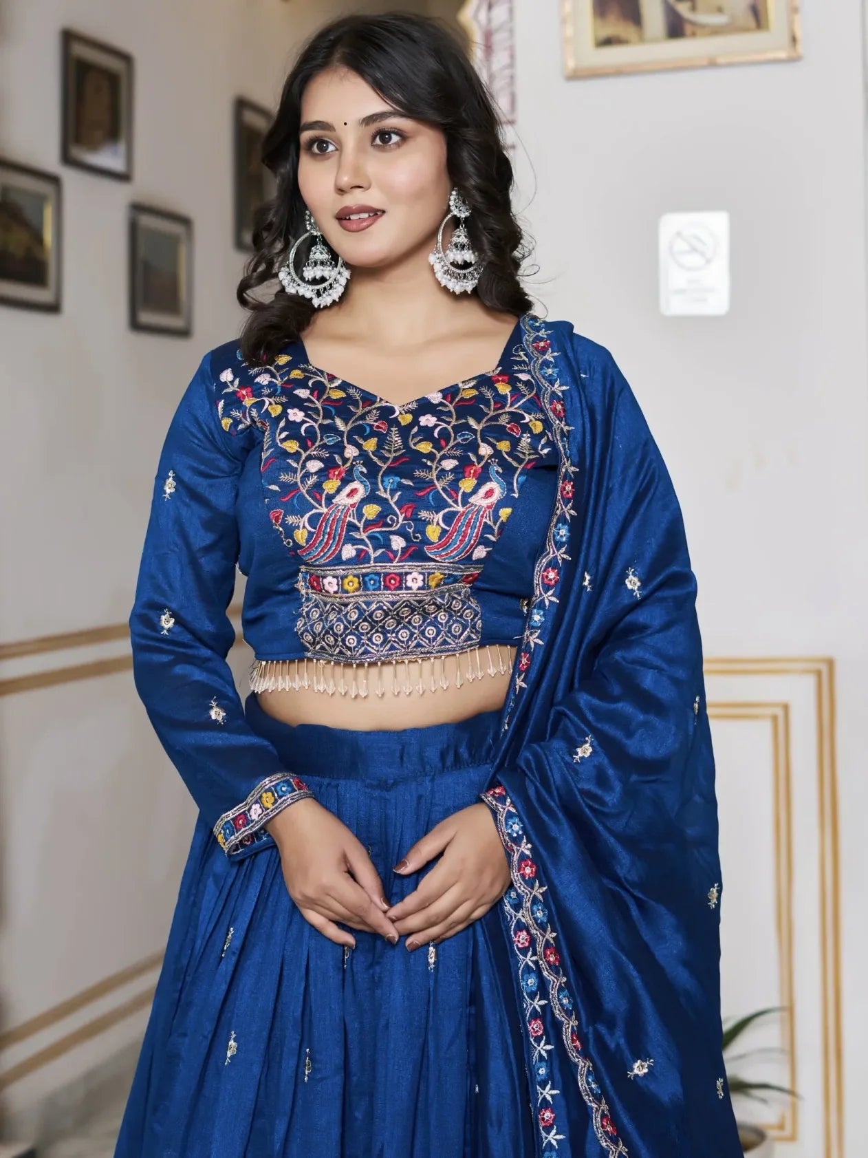 Woman wearing a traditional blue embroidered outfit indoors.