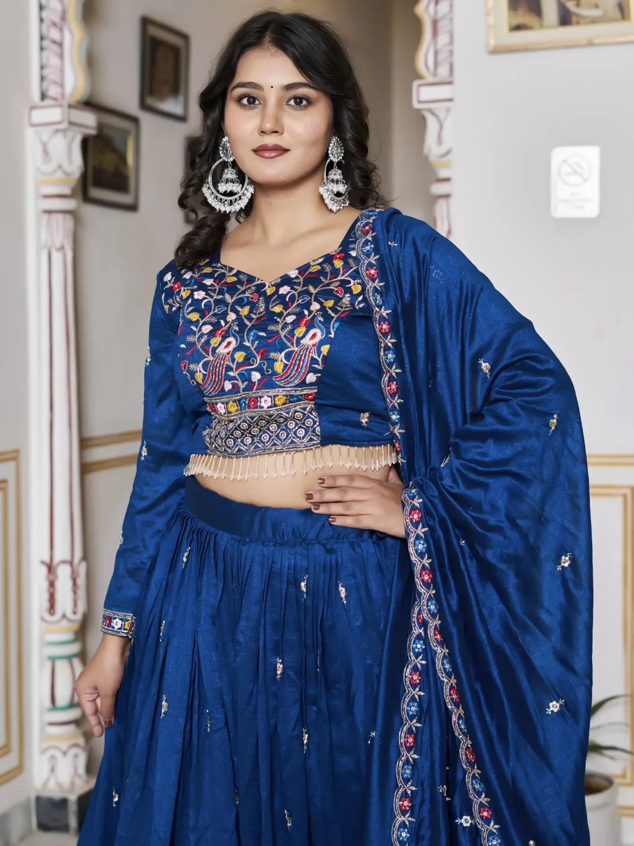 Woman wearing a traditional blue embroidered outfit indoors.