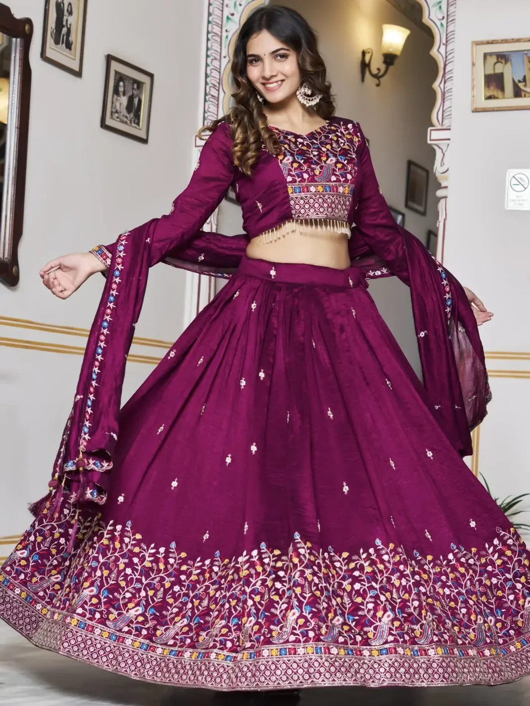 Woman wearing a purple traditional outfit with intricate designs in a decorated room.