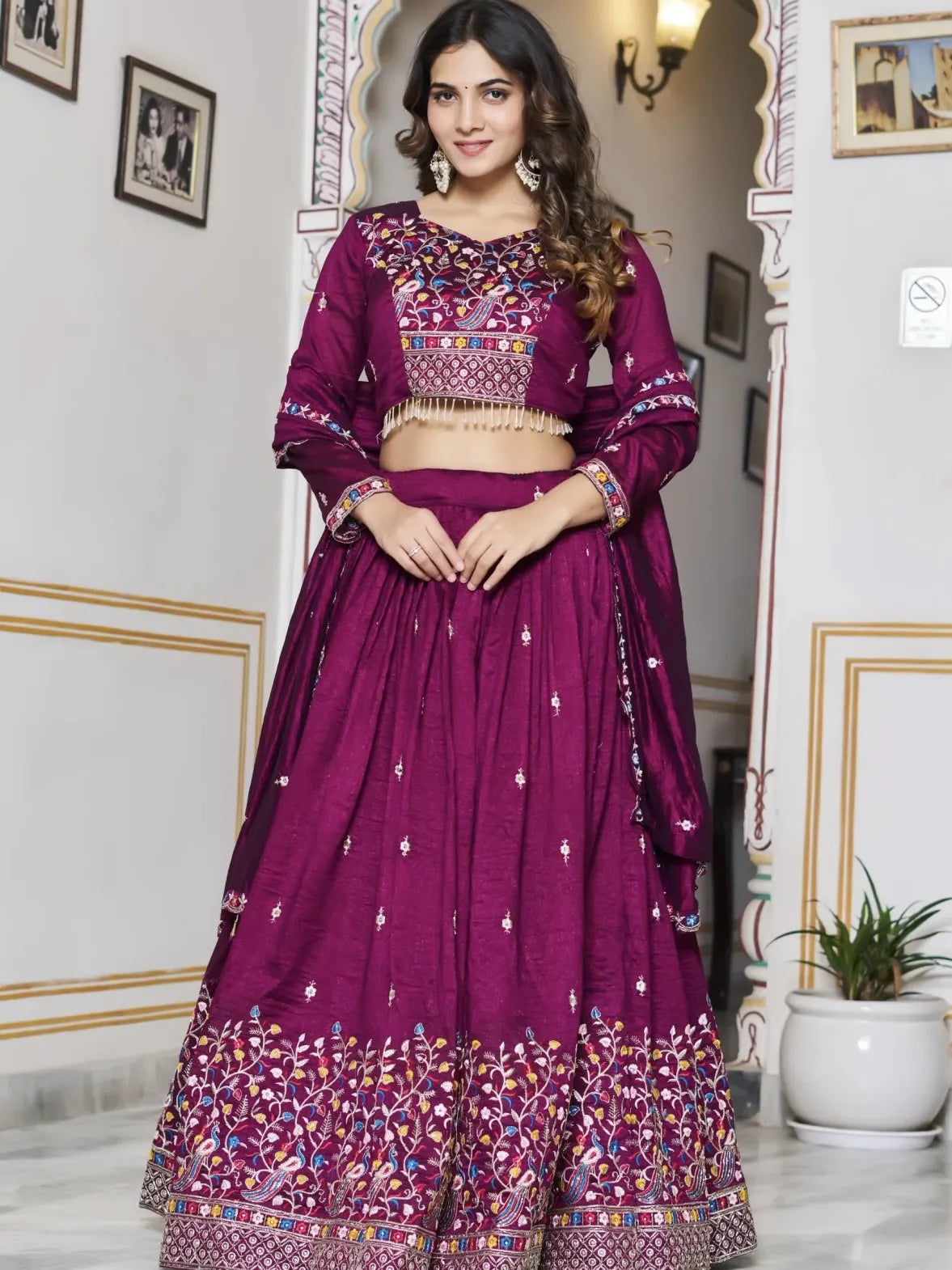 Woman in a purple embroidered traditional outfit standing in a decorated room.