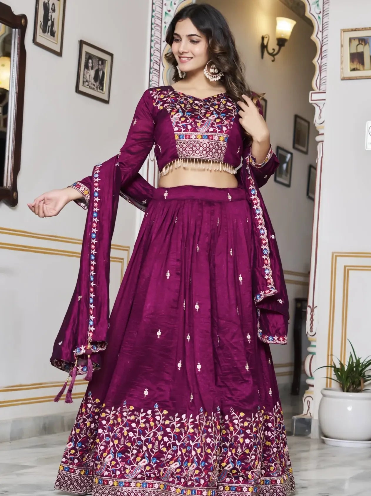 Woman in a traditional purple embroidered outfit standing in a decorated room.