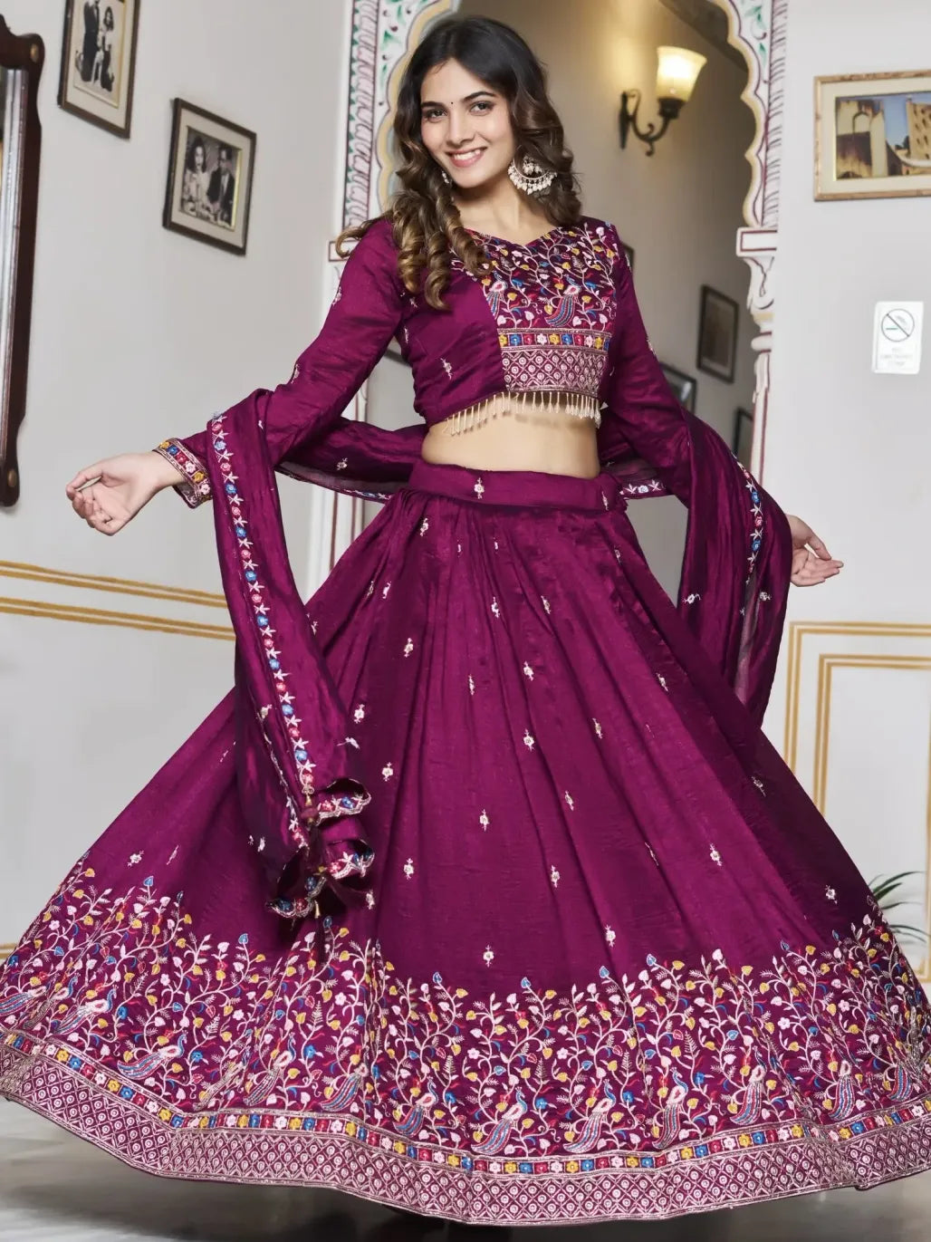 Woman in a purple embroidered traditional outfit standing in a decorated room.