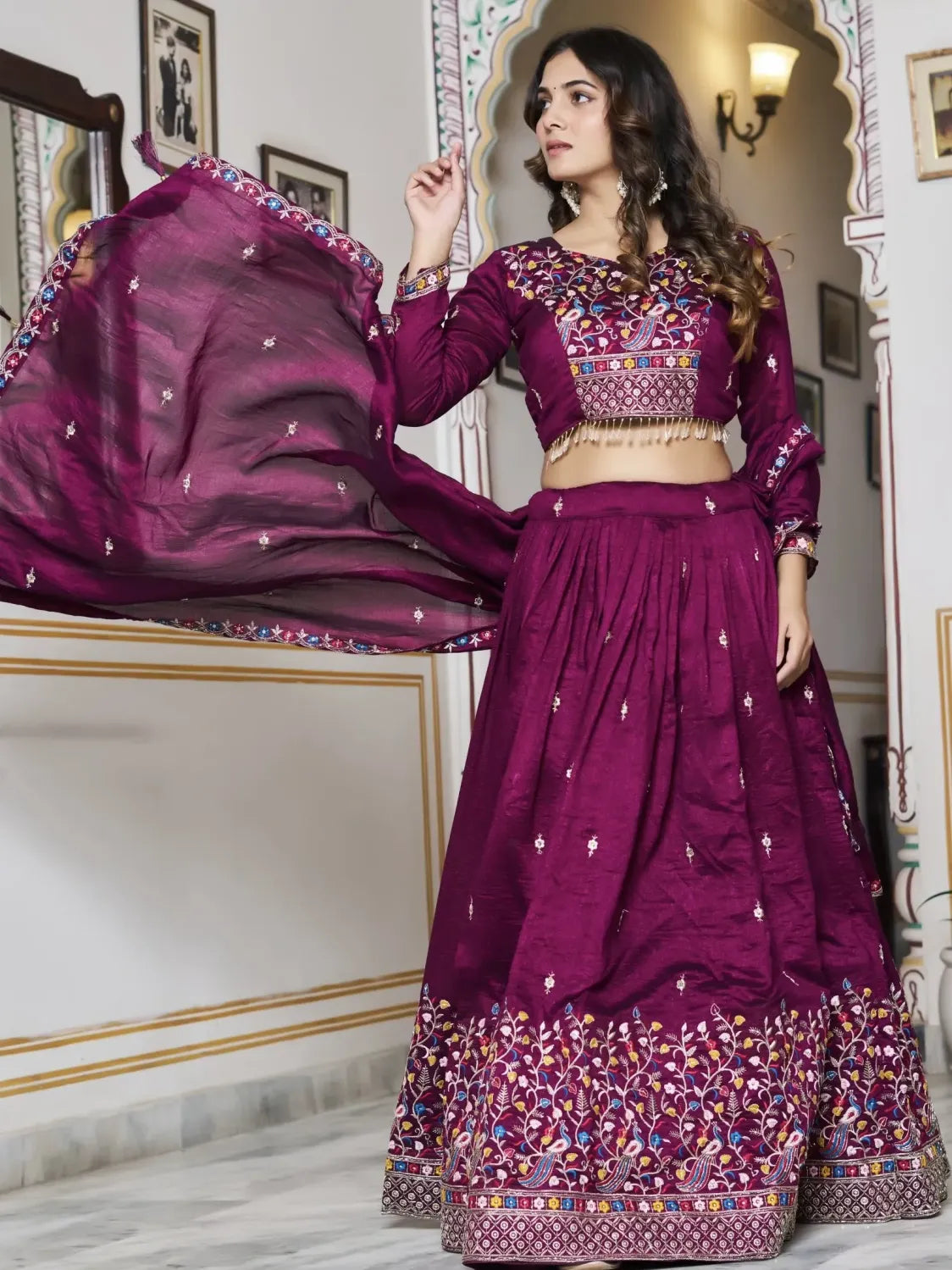 Woman in a traditional purple embroidered outfit standing in an ornate room.