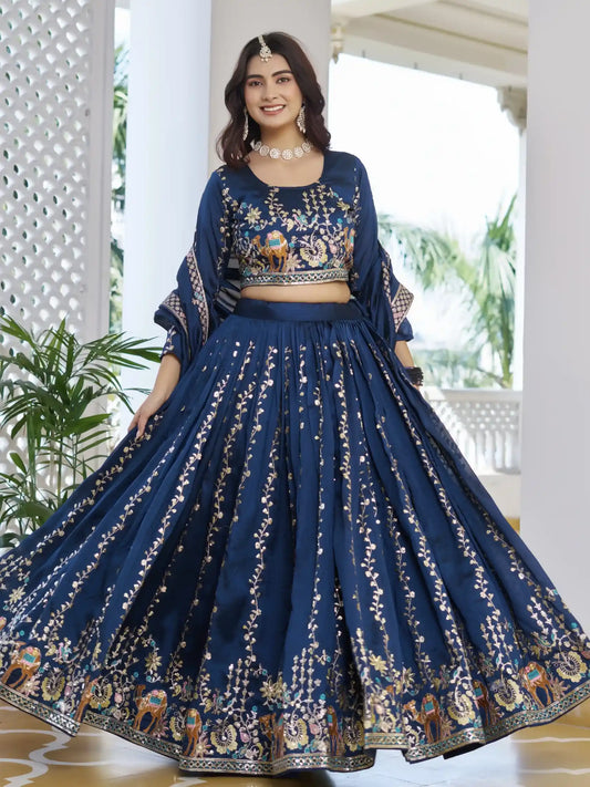 Woman wearing a traditional blue embroidered outfit indoors with plants in the background