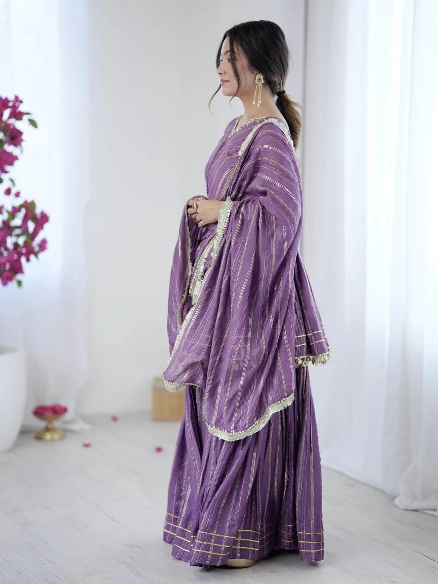 Woman wearing a purple traditional outfit with white patterns in a minimalistic setting.