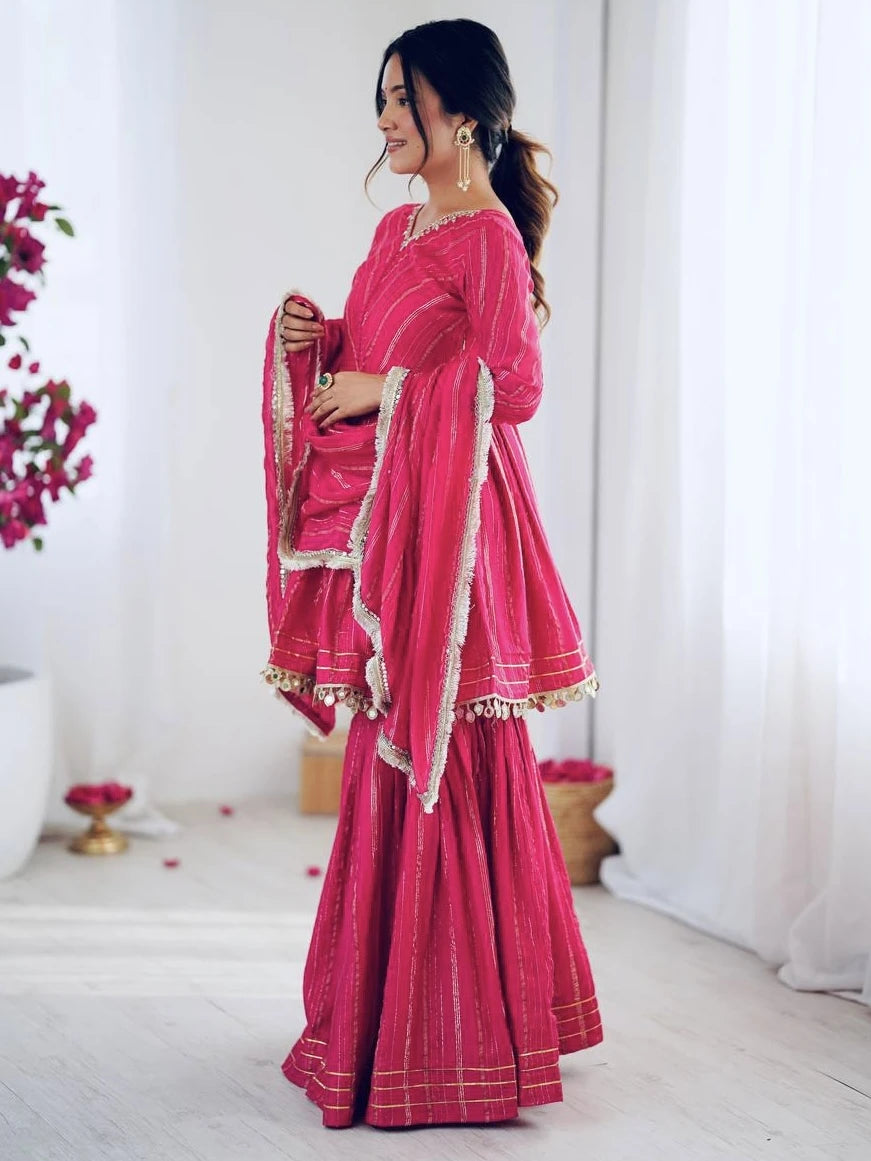 Woman wearing a pink saree with white patterns in a minimalistic setting.