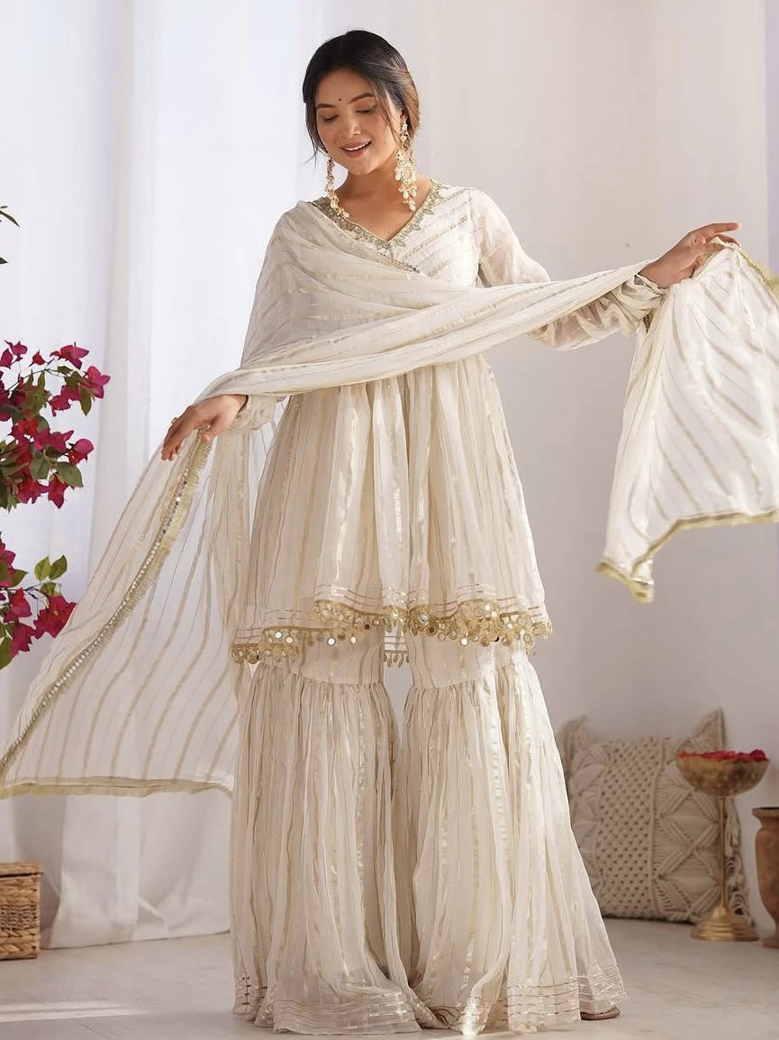 Woman in a cream traditional outfit with a matching dupatta in a bright room.