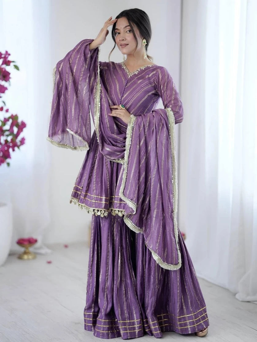 Woman wearing a traditional purple outfit with gold accents in a white room.