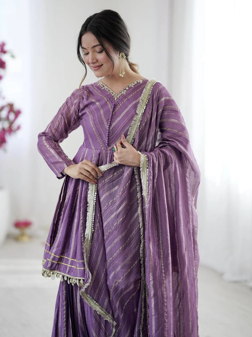 Woman wearing a purple traditional outfit with gold accents in a bright room.