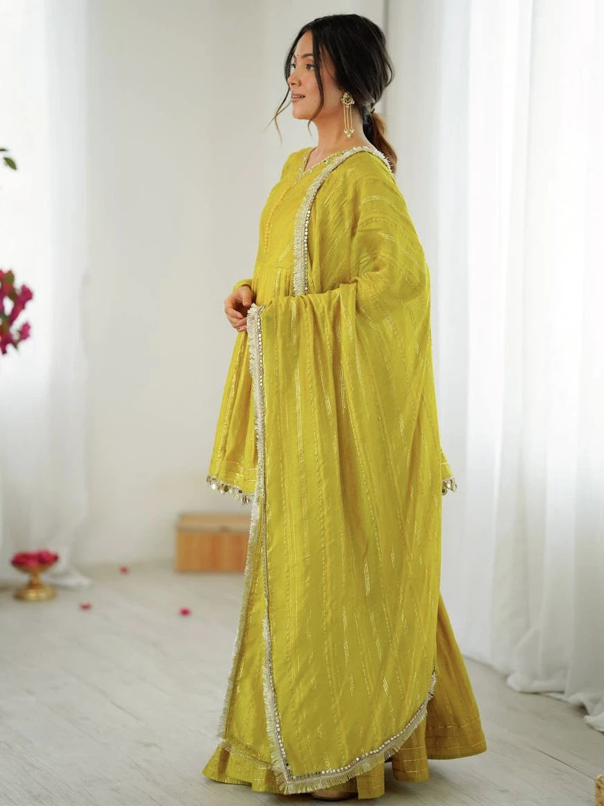 Woman wearing a yellow traditional outfit with white embroidery in a bright room.