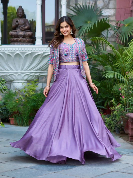 Woman in a purple traditional outfit standing outdoors with greenery and a statue in the background