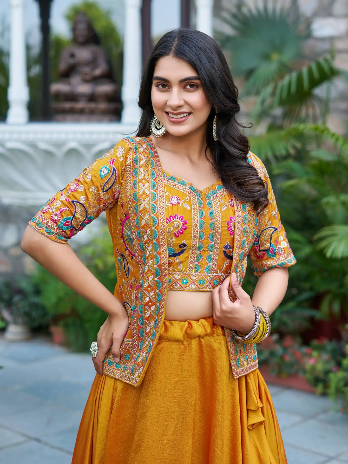 Woman in a traditional yellow outfit with intricate patterns standing outdoors.