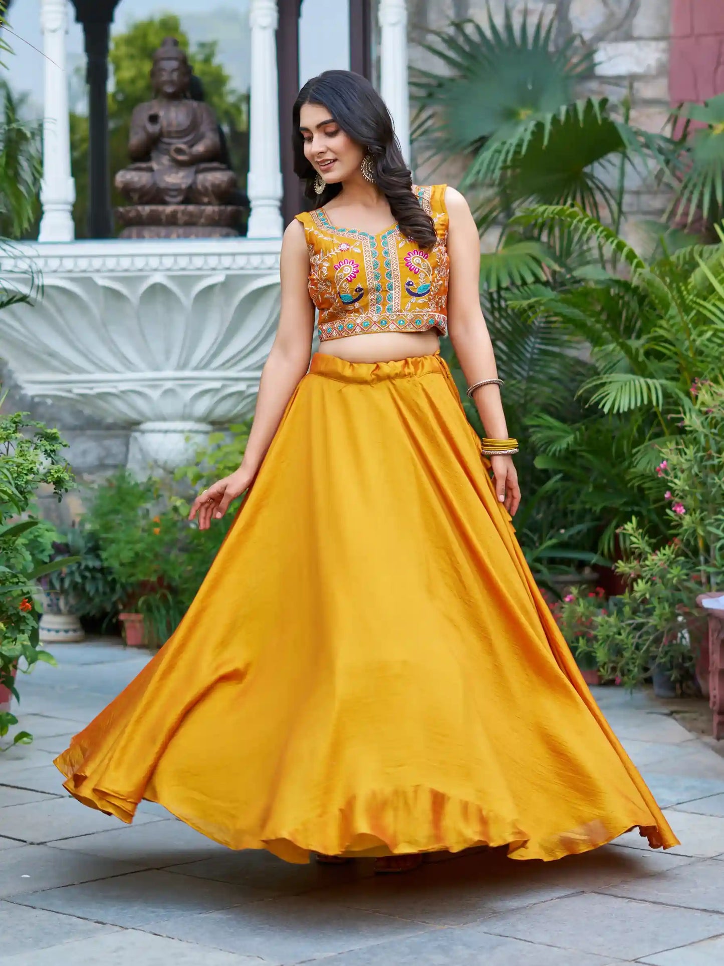 Woman in a yellow traditional outfit with intricate embroidery in an outdoor setting.