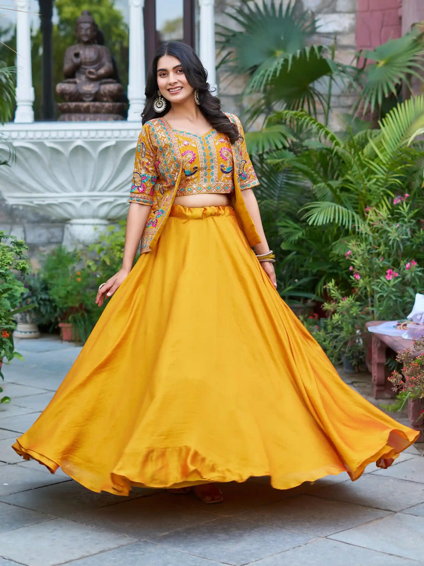Woman in a yellow traditional outfit with a patterned top, standing in a garden setting.