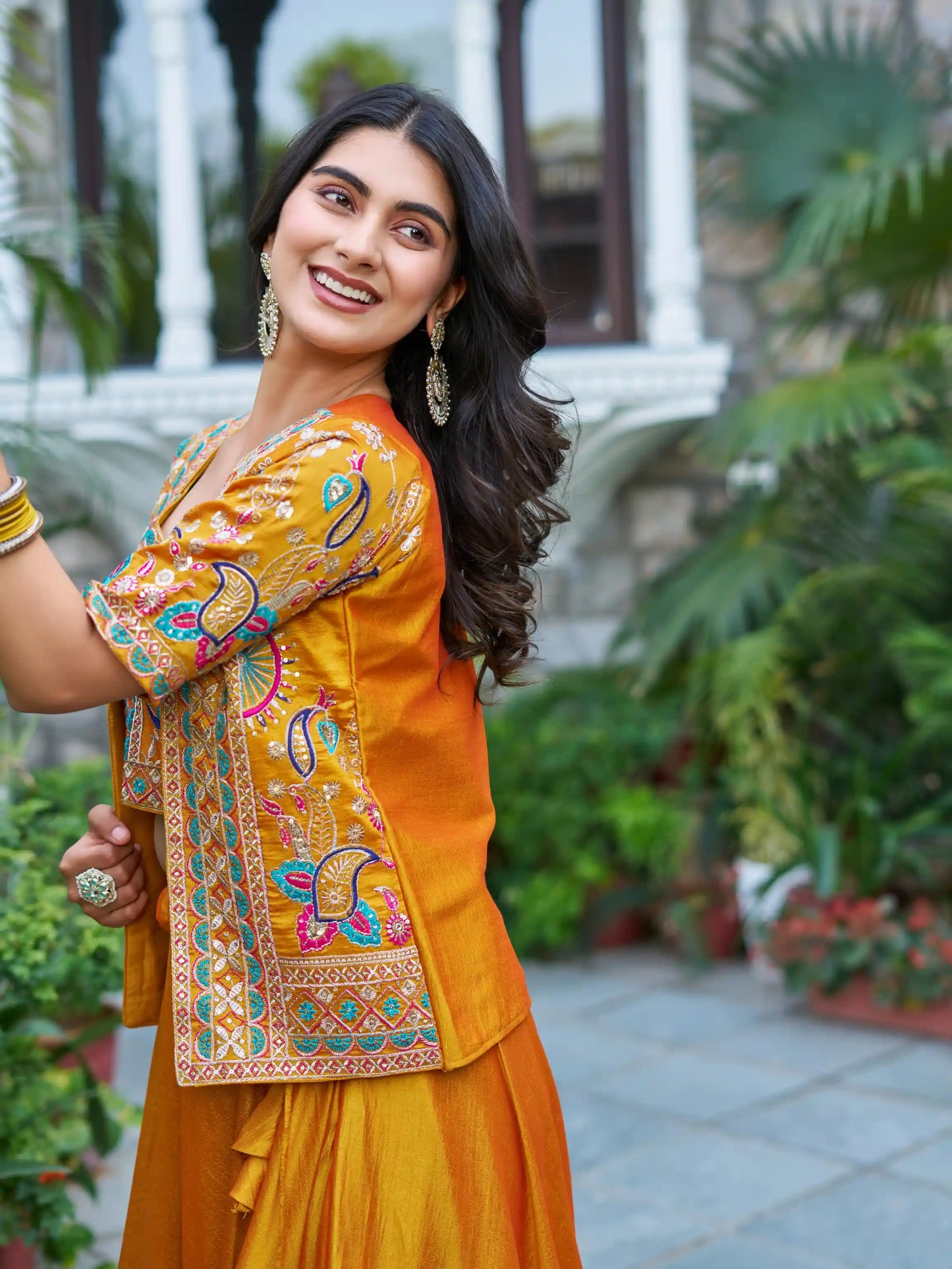 Woman wearing a traditional yellow outfit with intricate patterns in an outdoor setting.