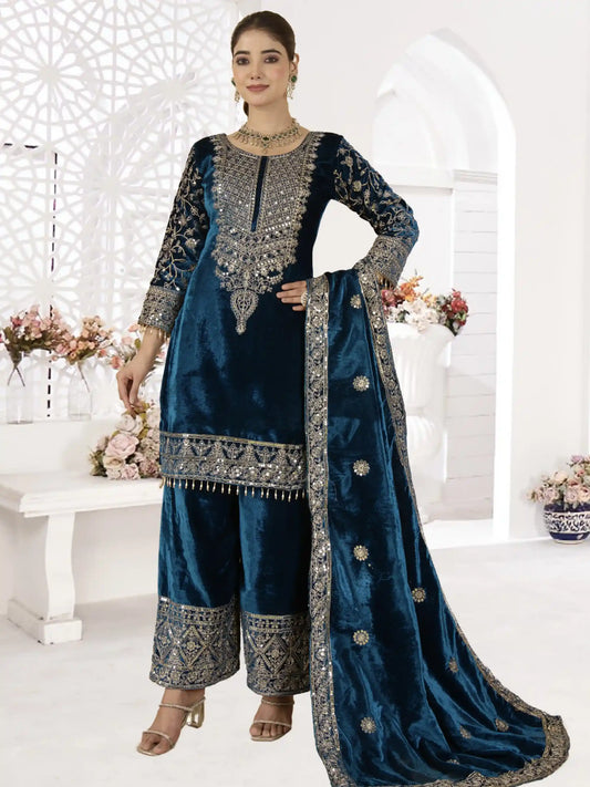 Woman wearing a blue embroidered traditional outfit in a white decorated room.