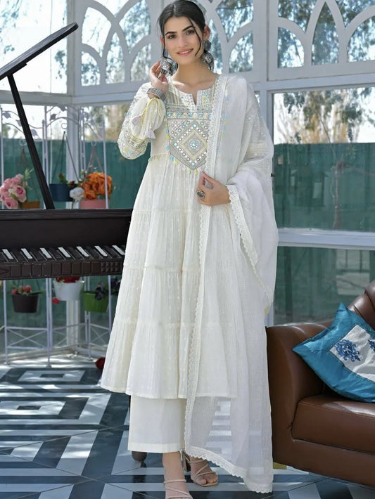 Woman in a white traditional outfit standing in a modern indoor setting with a couch and decorative items.