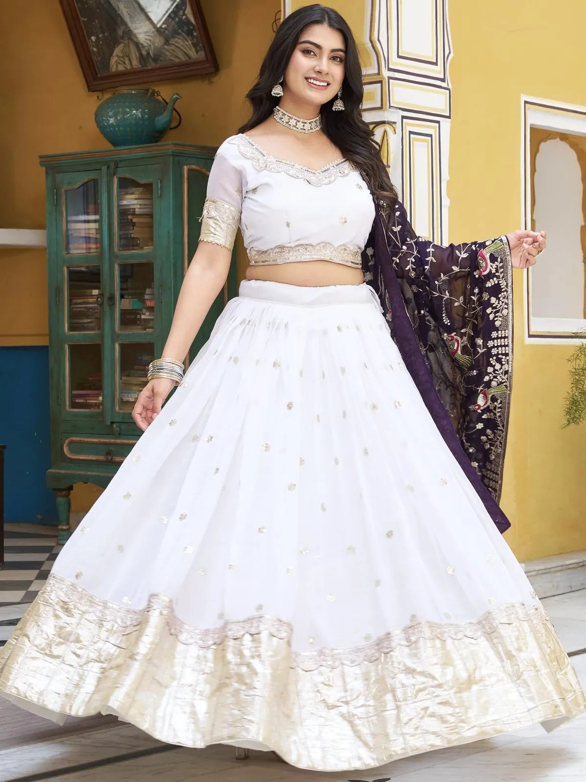 Woman in a white traditional outfit with gold details in an indoor setting.