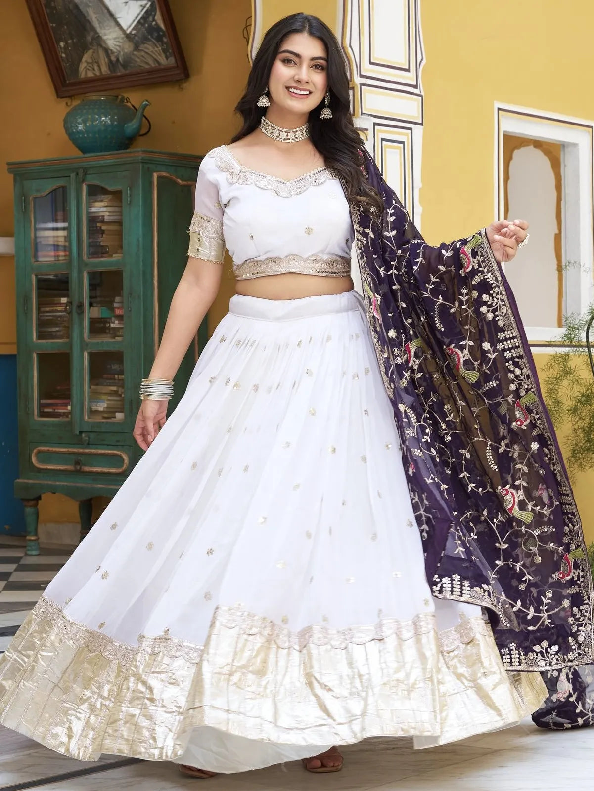 Woman in a white traditional outfit with a dark dupatta in a room setting