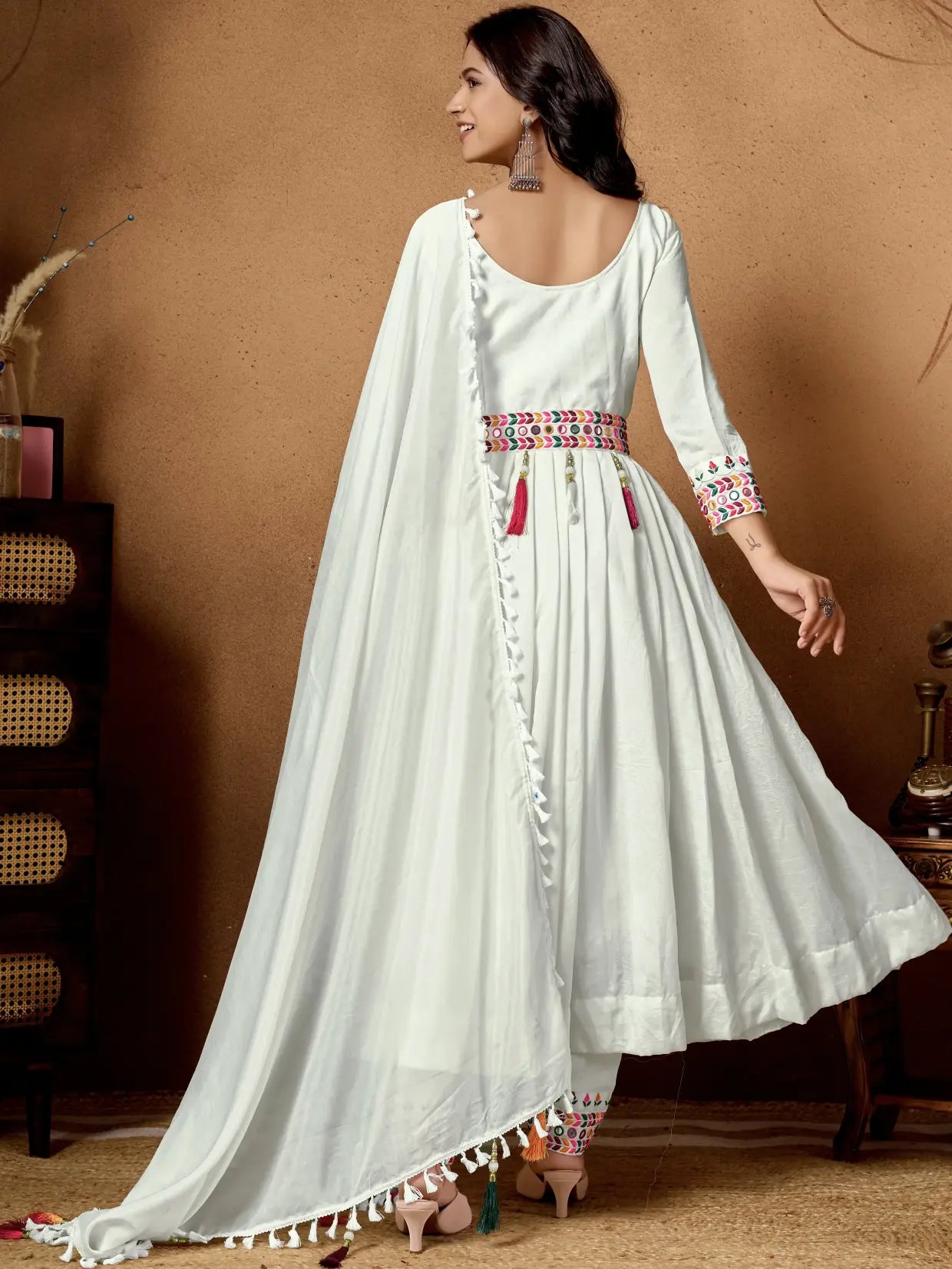 Woman wearing a white traditional outfit with colorful details against a brown background